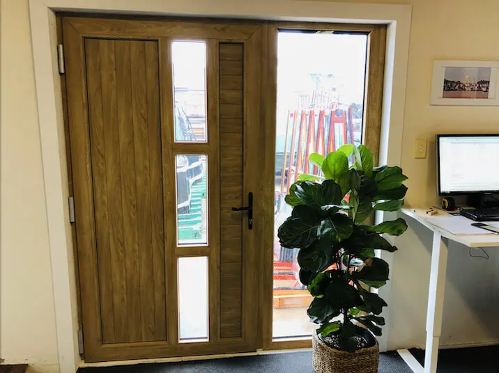 A wooden door with large glass panels, next to a potted plant and a computer desk.