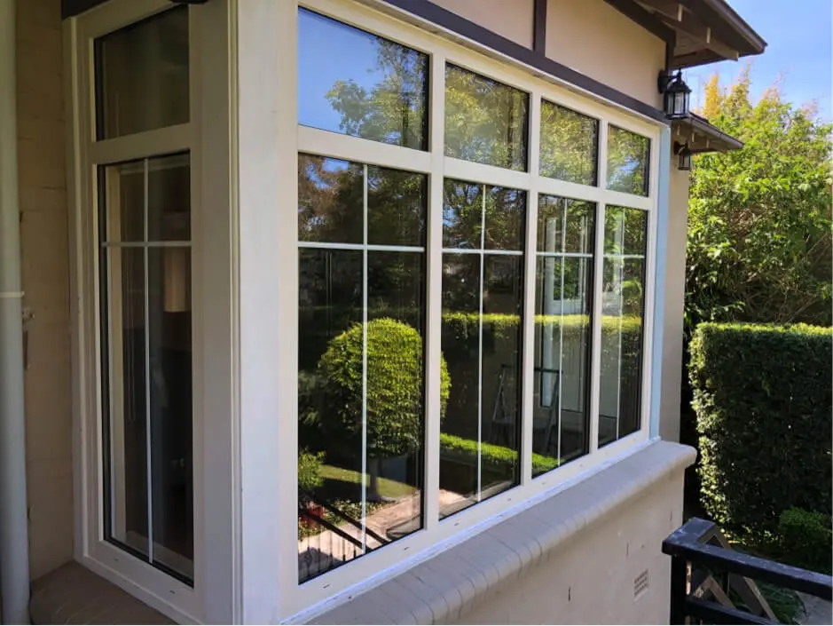 A large window with multiple panes showing greenery outside, a well-trimmed hedge, and a clear blue sky.