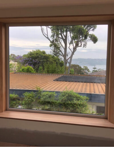 A wooden-framed window showcasing a view of distant trees and a calm body of water.